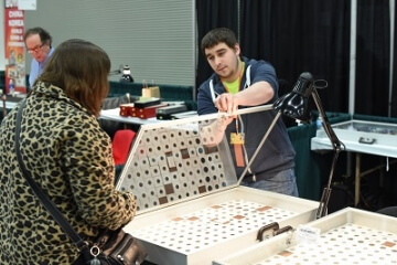 man opening a case at a coin show as a woman looks at the coins