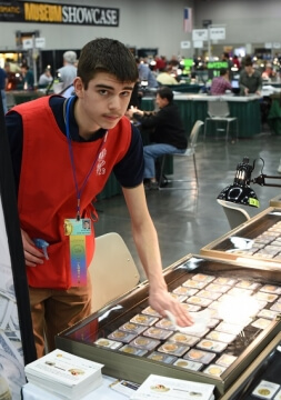 page standing by a booth at a coin show