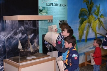 people looking at a model ship in a display case