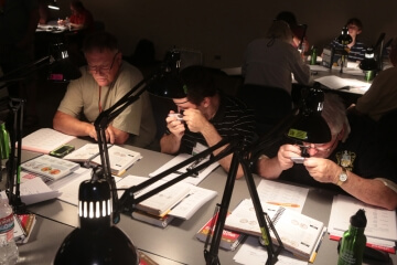 men at a table, one examining a coin