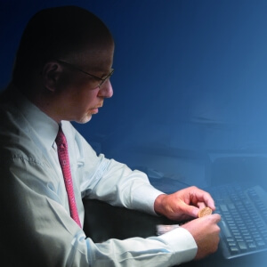man looking at coin, sitting in front of keyboard